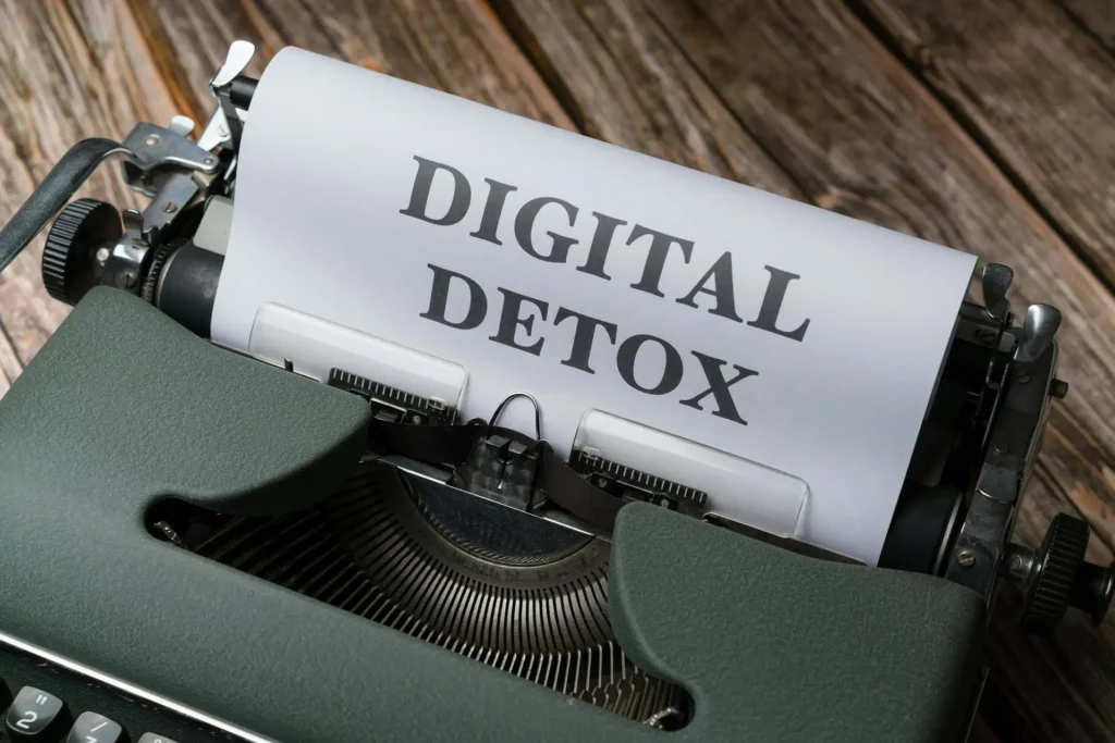 A vintage typewriter with a sheet of paper inserted, displaying the words Digital Detox in bold letters on a wooden surface.