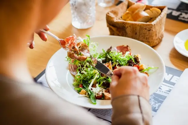 Person eating a balanced salad with leafy greens and protein, illustrating satisfying meals that may help reduce sugar cravings during a 30-day sugar detox plan.