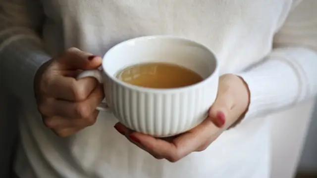 A person holding a warm mug of bone broth, representing daily habits for digestive wellness and gut barrier support.