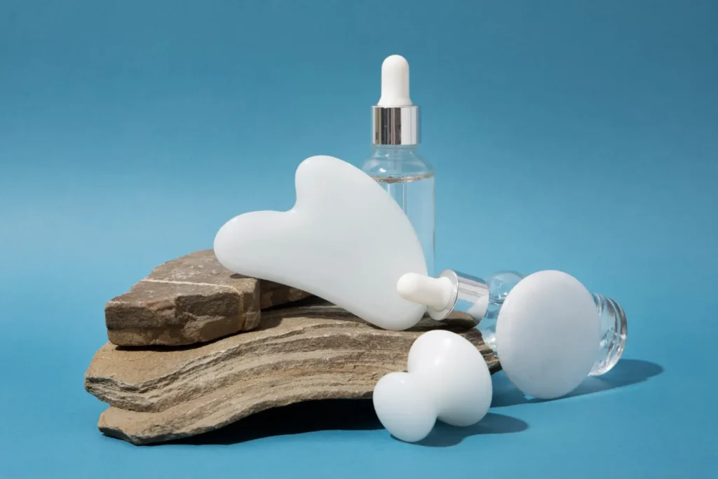 Minimalist product display featuring white facial massage tools and glass serum dropper bottles arranged on natural stone against a blue background, representing advanced anti-aging peptide skincare focused on cellular repair beyond collagen