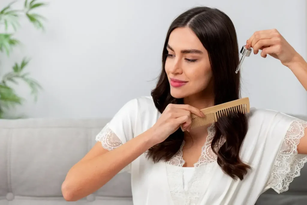A woman applying a natural serum to her dark hair using a dropper and a wooden comb, illustrating the application of Foliprime for hair growth to support scalp health and restoration.