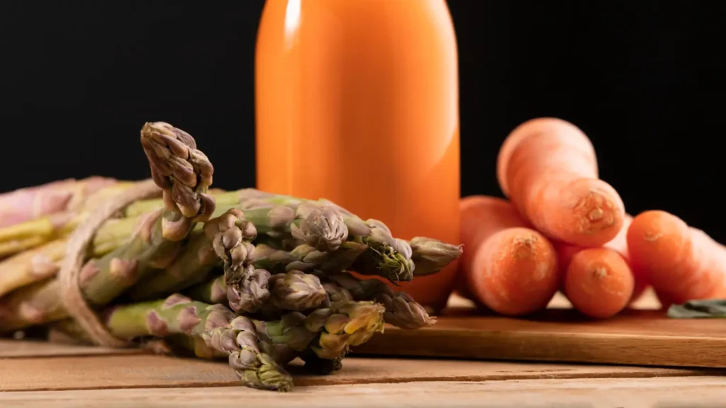 Fresh asparagus and carrots beside a bottle of natural vegetable juice, representing nutrient-rich foods and natural ingredients associated with GLP-1 support, appetite control, and healthy weight loss.