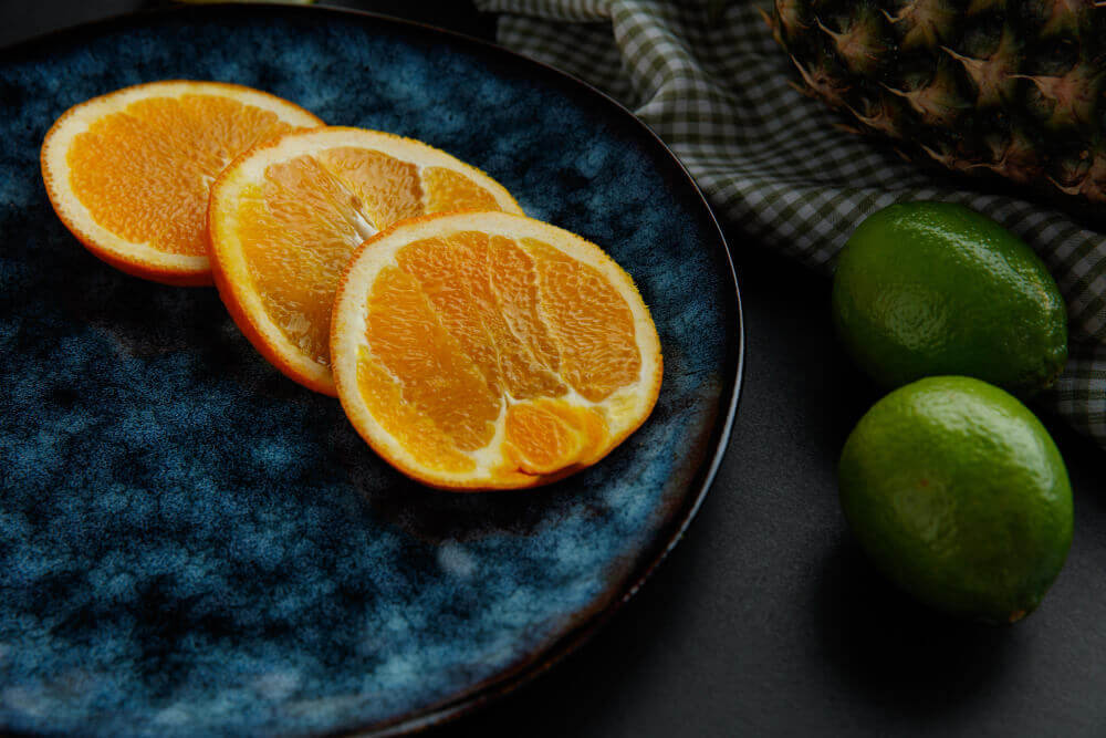 Fresh sliced oranges on a dark plate with limes and pineapple in the background, representing citrus-burn review based ingredients commonly used in fat-burning and metabolism-boosting supplements.
