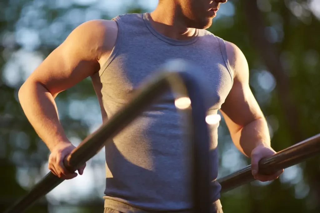 Muscular man exercising outdoors on parallel bars at sunset, highlighting strength, stamina, and male vitality associated with natural Endopeak review testosterone support supplements.