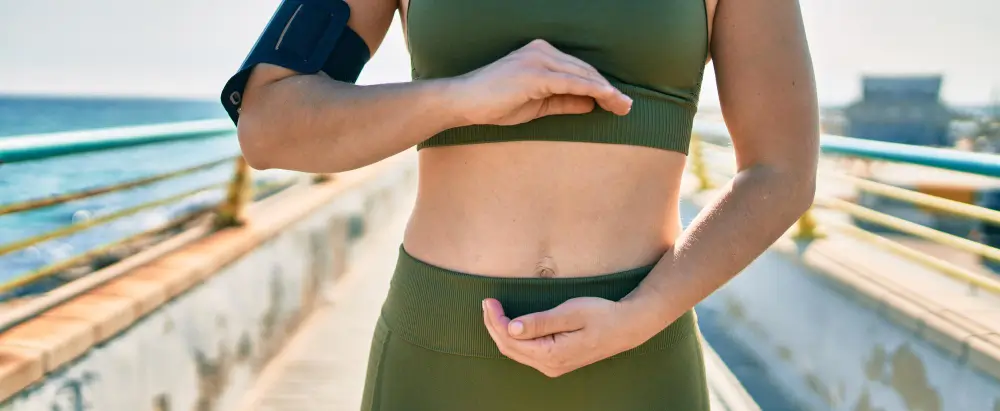 Liv Pure Review of a Fit woman outdoors holding her abdominal area, symbolizing liver health, metabolism support, and natural fat-burning associated with detox and weight management supplements.