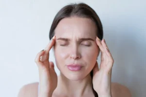Woman experiencing mild discomfort and headache, representing adjustment symptoms after dietary changes, including fatigue, cravings, digestive shifts, and adaptation to a healthier eating pattern.