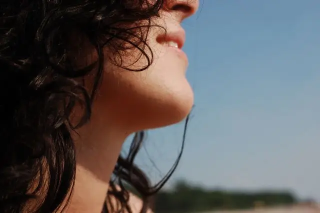 Close-up profile of a smiling woman outdoors in the sunlight, illustrating how skin ages due to extrinsic factors like UV radiation.
