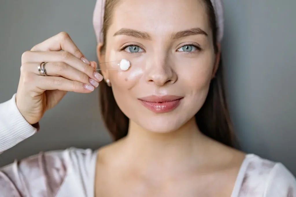 Woman applying facial serum to her face, illustrating a skincare routine with retinol vs. bakuchiol.
