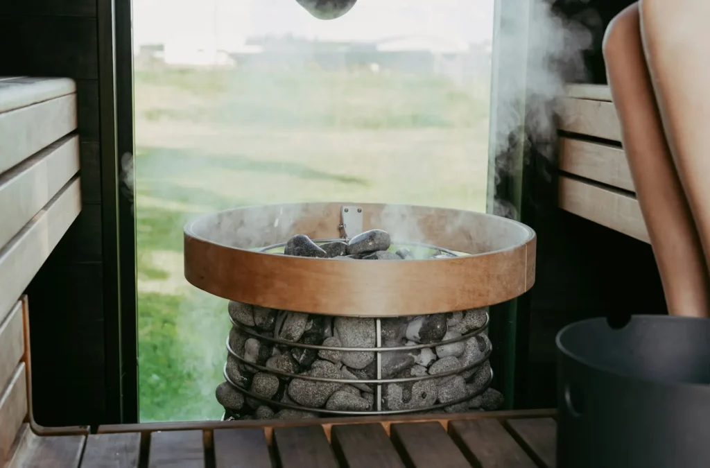 Steam rising from hot sauna stones inside a modern sauna, representing sweat therapy benefits, sauna exercise research, muscle recovery, circulation, and overall wellness.