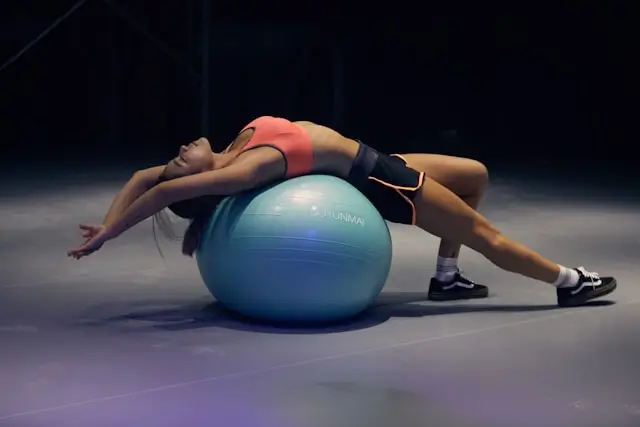 Woman performing a low-impact stability ball exercise to improve core strength, balance, flexibility, and recovery as part of a sustainable detox fitness routine.