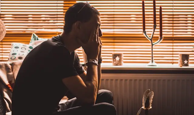 Man sitting alone with his head in his hands, illustrating signs sometimes associated with stress-related low testosterone, including fatigue, low mood, and reduced energy.
