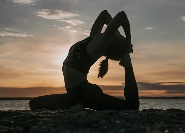 Woman practicing a yoga pose at sunrise by the ocean, illustrating the physical and mindfulness benefits of walking yoga.