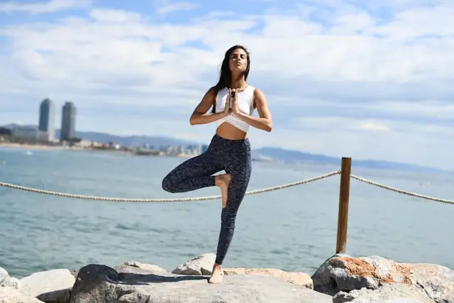 Woman practicing mindful movement by the seaside in a balanced yoga pose, representing walking meditation, mindfulness, and the mind-body connection in walking yoga.