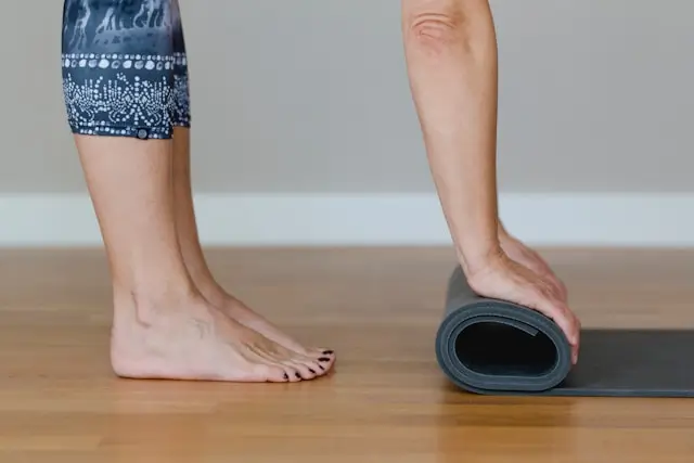 Person barefoot beside a rolled yoga mat, illustrating walking yoga and gentle movement practices that combine walking, stretching, balance, and mindful exercise.